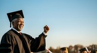 Male graduate in academic regalia celebrating achievement outdoors with clear sky background, suitable for education, graduation, success, and milestone content.