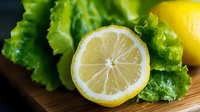 Fresh lemon half with green lettuce leaves on wooden cutting board. Healthy cooking ingredients for salads and organic food preparation in kitchen.