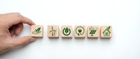 Hand placing wooden blocks with green eco icons including wind, solar, and plant symbols, representing sustainable energy concepts on white background.