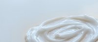 White cream swirl texture on light background for skincare cosmetic product design and beauty advertising applications.