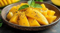 Fresh mango chunks with chia seeds and mint leaves in rustic wooden bowl, tropical fruit dessert for healthy eating.
