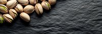 Fresh roasted pistachio nuts scattered on dark slate stone background with copy space, top view panoramic banner format for food design.