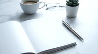 Open notebook with blank pages on marble desk with coffee cup, eyeglasses, succulent plant, and pen for business, creative writing, planning, or office workspace design projects.