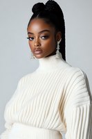 Young African American woman in white turtleneck sweater with braided updo hairstyle and statement crystal earrings against gray background, fashion portrait.