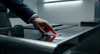 Professional businessman hand inserting red access card into modern security scanner at corporate office entrance for employee identification and building access.