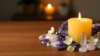 Burning candle surrounded by healing crystals and gemstones on wooden surface creating peaceful meditation atmosphere for wellness and spiritual practices.