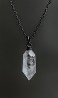 Clear quartz crystal pendant on black chain necklace with wire wrapping against dark background for jewelry and accessories design.