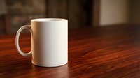 White ceramic coffee mug on wooden table surface with warm lighting and blurred background for mockup design and branding projects.