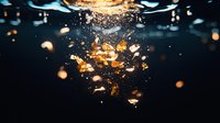 Dramatic underwater explosion with golden particles and bubbles creating dynamic motion effect against dark background. Artistic macro photography for creative projects.