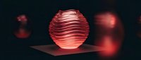 Red metallic sphere with horizontal ridged texture on dark platform with ambient lighting effects for modern design projects.