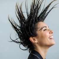 Young Hispanic woman with wet hair in dynamic motion against gray background expressing joy and freedom through movement.