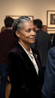 Elegant mature African American woman in black blazer at art gallery opening with braided updo hairstyle smiling confidently among crowd of visitors.