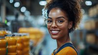 Young African American woman with natural curly hair and glasses smiling warmly in casual attire. Bright authentic portrait with soft bokeh background showing genuine happiness.