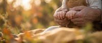 Senior man meditating outdoors in autumn park with golden sunlight and falling leaves creating peaceful wellness atmosphere for relaxation and mindfulness.