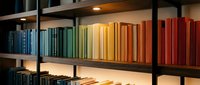 Colorful books arranged by rainbow spectrum on modern library shelves with warm lighting creating cozy reading atmosphere for education and learning.