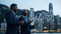 Two businessmen in suits analyzing digital financial charts and market data on transparent displays against evening city skyline with illuminated buildings.