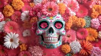 Decorated sugar skull with floral pattern surrounded by pink gerbera daisies, orange marigolds and white chrysanthemums on pink background. Day of Dead celebration.