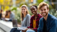 Diverse group of young adults smiling outdoors on campus, enjoying social interaction during break from studies with laptop and books.