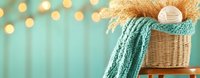 Cozy winter composition with knitted turquoise scarf on wicker basket, warm lights bokeh background creating festive holiday atmosphere.