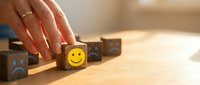 Woman hand selecting wooden cube with happy smiley face among sad faces on desk, positive thinking and customer satisfaction concept for business.