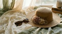 Cozy bedroom scene with straw sun hat, sunglasses and coffee cup on rumpled bed linens. Warm morning light creates relaxing vacation atmosphere for lifestyle content.