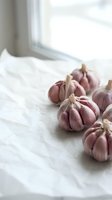 Fresh purple garlic bulbs arranged on white marble countertop in bright kitchen with natural window light for culinary cooking and food preparation.