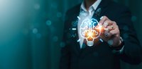 Professional businessman touching glowing lightbulb with digital innovation icons representing creative business solutions and technology advancement.