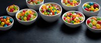 Colorful candy assortment in ceramic bowls on dark surface for confectionery business, party planning, and sweet treat marketing materials.