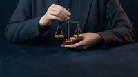 Professional lawyer or judge holding golden scales of justice in dark formal setting representing legal system and courtroom proceedings.