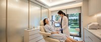 Modern dental office interior with female dentist examining patient in treatment chair with advanced equipment and natural lighting.