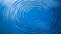 Concentric ripples expanding outward on calm blue water surface creating mesmerizing circular pattern with gentle waves and tranquil aquatic motion.