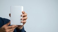 Man holding blank white box or package in hand against neutral background for product mockup and branding purposes.