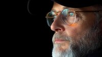 Senior Caucasian man with gray beard and round glasses in dramatic side profile lighting against dark background, contemplative expression and thoughtful gaze.