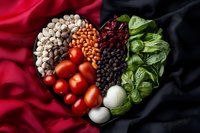 Fresh ingredients arranged in heart shape with beans, tomatoes, mushrooms, lettuce and garlic on dramatic red and black fabric background for healthy cooking concept.