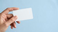 Hand holding blank white business card against light blue background for branding, corporate identity, and marketing mockup purposes.