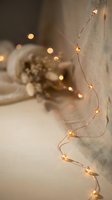 Warm golden fairy lights draped on beige linen fabric creating cozy ambient lighting with soft bokeh background for home decor and seasonal celebrations.