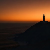 Lighthouse silhouette on coastal cliff at golden sunset over ocean horizon creating dramatic seascape for travel and navigation themes.