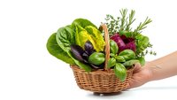 Fresh organic vegetables and herbs in wicker basket held by hand on white background. Healthy eating, farm produce, cooking ingredients concept.
