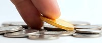 Close-up of hand holding golden coin above scattered silver coins on white surface, symbolizing wealth, investment, savings, and financial success for business concepts.