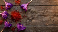 Purple crocus flowers and saffron spice threads arranged on rustic wooden background for culinary and botanical themes.