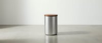 Stainless steel cylindrical container with wooden lid on neutral surface, suitable for product packaging and kitchen storage design projects.