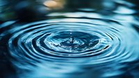 Macro shot of water drop impact creating concentric ripples on blue water surface with dramatic lighting and dark background. Captures moment of splash.