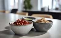 Assorted spices and seasonings in rustic ceramic bowls on marble countertop, modern kitchen setting for culinary preparation.