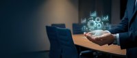 Businessman holding holographic digital technology icons with gears and data analytics floating above hands in modern office environment for business innovation.