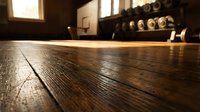 Empty gymnasium with polished wooden floor, basketball hoop, and windows casting natural light. Low angle perspective emphasizing floor texture for sports facility and athletic venue concepts.