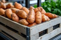 Fresh organic sweet potatoes in wooden crate at farmers market, raw natural produce for healthy cooking and seasonal harvest display.