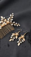 Elegant gold bridal jewelry set with floral hair comb and matching earrings featuring pearls and leaves on dark fabric background for wedding accessories.