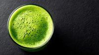Fresh matcha green tea latte with foam in glass on dark slate background, healthy antioxidant drink for wellness and energy boost.