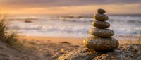 Zen stone stack balanced on beach rock at golden sunset with ocean waves and warm light creating peaceful meditation atmosphere for wellness and mindfulness concepts.