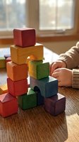 Child playing with colorful wooden building blocks stacked on table near window. Educational toy development and creative learning activity concept.